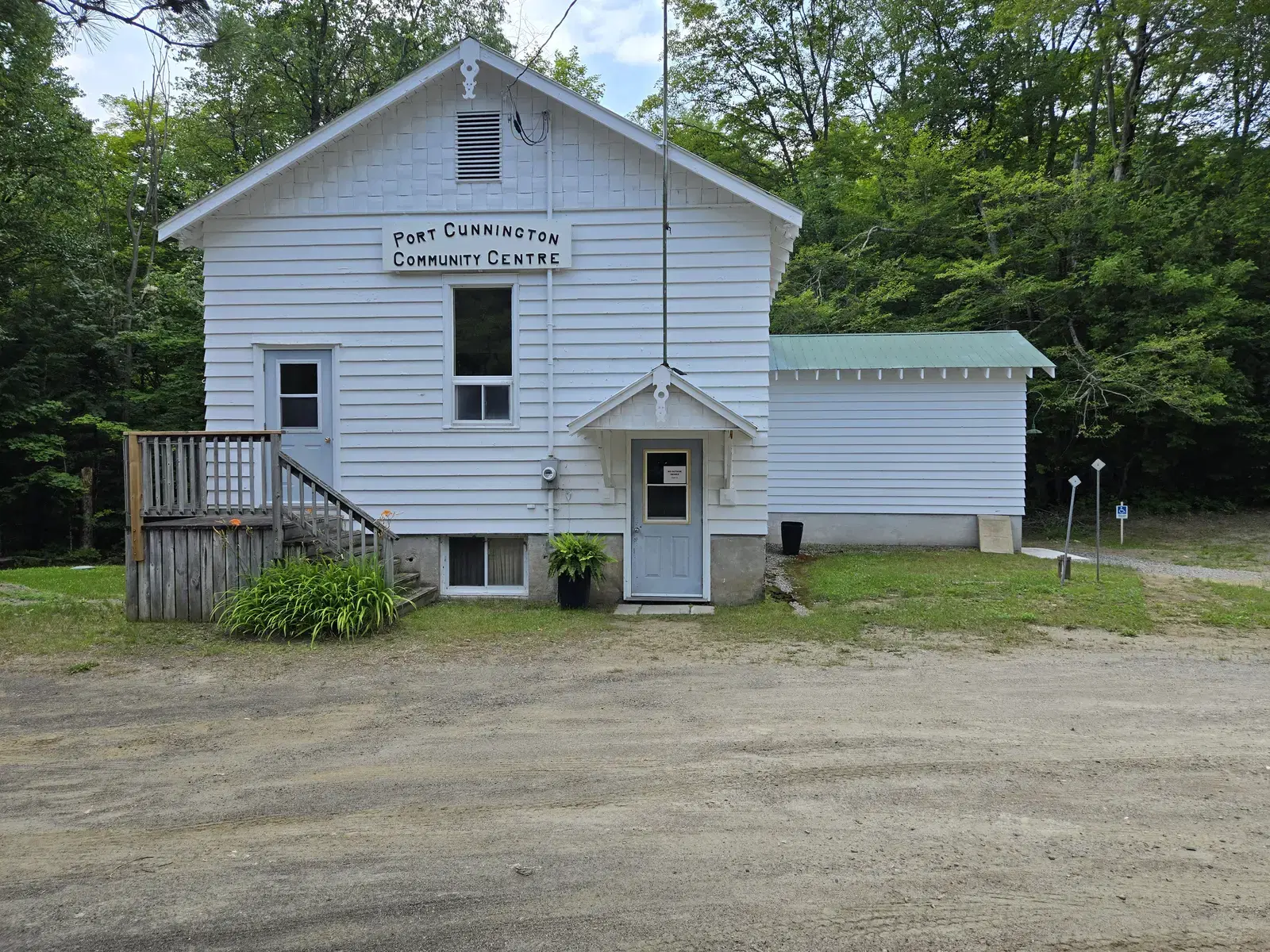 The front of the community centre: white clapboard, a small covered porch over the pale blue door, and a wooden ramp and steps to the left.